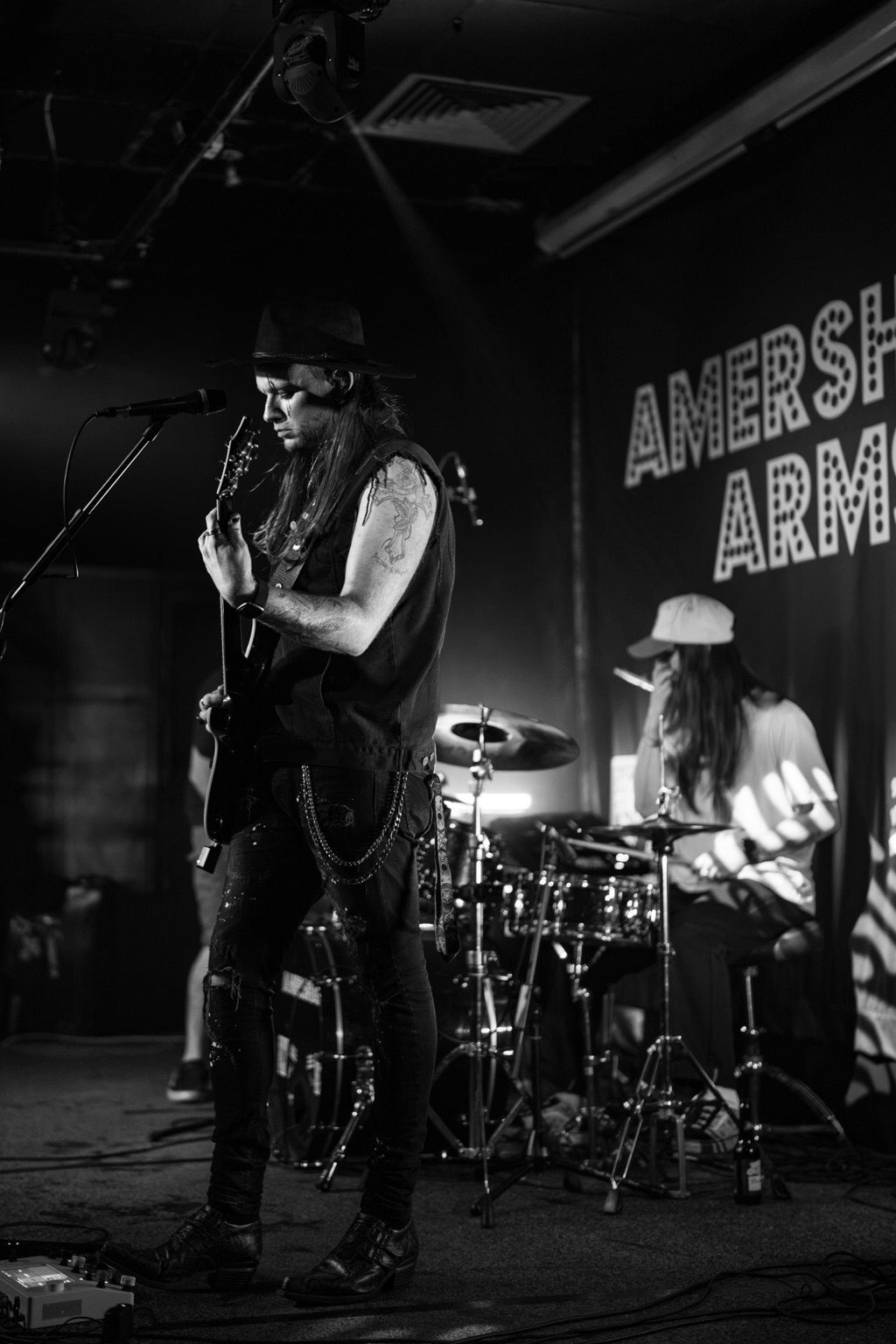 Steven Speck playing guitar at the microphone with Cameron Jessop on drums behind him, both performing live